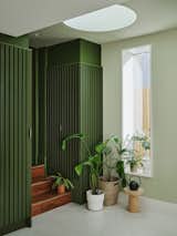 The kitchen of this London home is accessed via the main entrance hall, down three steps made from a dark timber that echoes the cherry wood cabinetry. The stairs are framed by green slatted cabinets finished in Jewell Beetle paint by Little Greene.