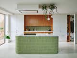 The new kitchen features green kit kat tiles, a terrazzo-effect rubber floor, white cabinetry, and cherry wood veneered cabinets. The client originally wanted teak cabinets, but 4 S Architecture recommended using cherry wood instead as it is more sustainable but has the same warm tones as teak. “We couldn’t get behind teak as a product so we used FSC certified European cherry that has less air miles than American cherry,” explains architect Julia Hamson. “The client was really pleased with the result.”